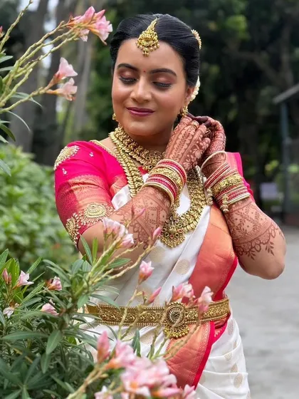 Our beautiful bride Sahana getting ready for her muhurtham. She chose a classic Kasu haram (coin necklace) layered with a choker, all in a traditional gold finish that perfectly matches her white and pink Kanjeevaram saree.