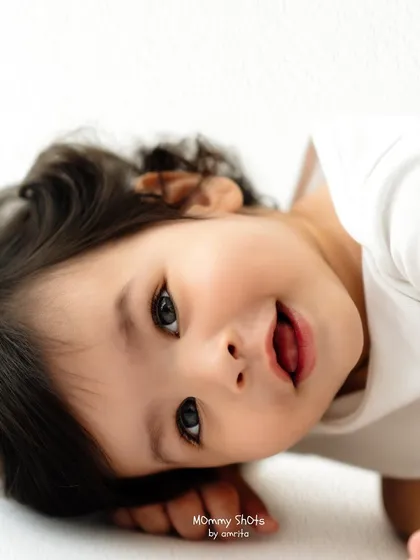 A playful, high-key portrait of a baby lying on their side, capturing a moment of pure joy.