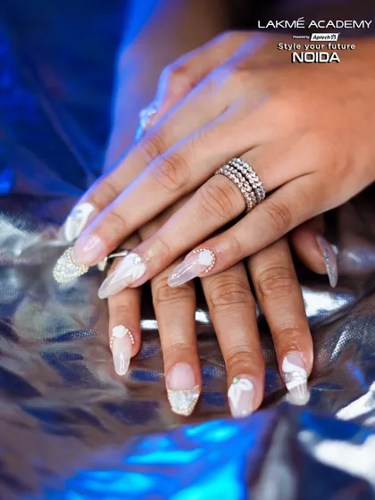 A full view of a completed set of sculpted gel nails with white ribbon details and silver glitter accents. This style requires precision in both extension application and decorative work, which we cover extensively.