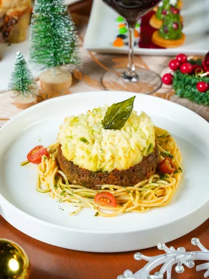 A festive plate of spaghetti with a meatball patty, styled with mini Christmas trees and ornaments. This shot creatively incorporates holiday elements into a classic dish.