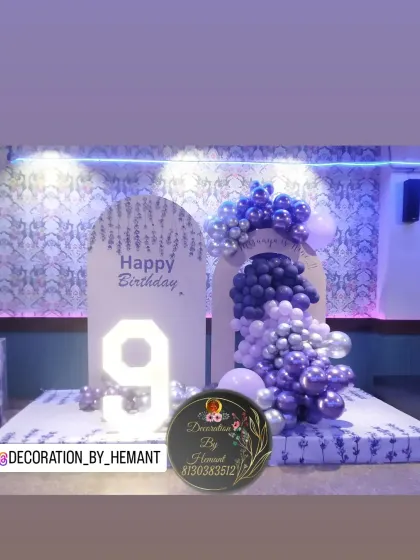 A stylish and modern stage setup for a 9th birthday. The decor includes two arched backdrops, a cascading balloon arrangement in shades of purple and silver, and a large light-up marquee number '9'.