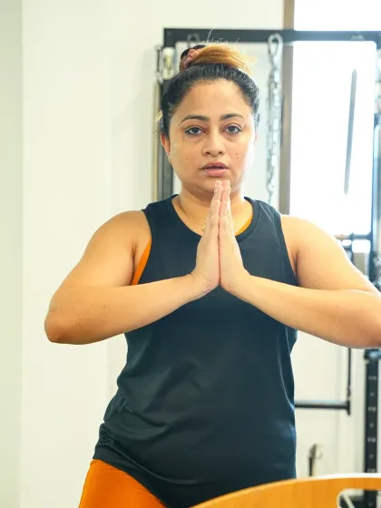 A client holds a graceful prayer squat, a position that challenges balance and builds lower body strength. The focus and calm on her face reflect the mindful nature of Pilates.