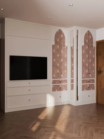 The custom wardrobe in this bedroom features traditional Indian arched motifs on the doors, blending seamlessly with the room's overall aesthetic. The unit also incorporates a media console for the TV.