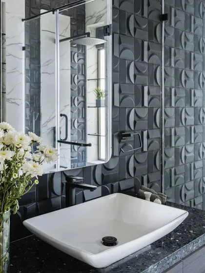 This bathroom uses 3D geometric tiles in a dark grey to create a highly textural and modern feature wall. The clean lines of the white vessel sink and black countertop provide a crisp contrast.