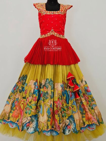 A grand layered gown with a Kalamkari print. The red peplum top is paired with a yellow skirt featuring a vibrant, story-like print.