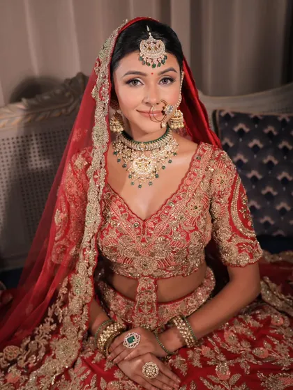 A smiling bride in her traditional red lehenga. The makeup is designed to enhance her happiness, with glowing skin and eyes that sparkle.