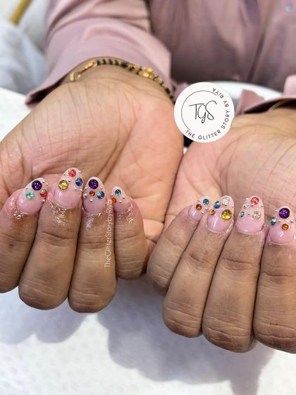 A playful and colorful crystal manicure. This set features a sheer pink base with a variety of large, colorful gems placed near the cuticles for a fun and bold look.