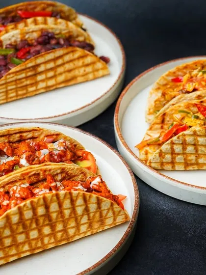 A delicious spread of assorted tacos, showcasing different fillings like paneer, chicken, and beans, served on three separate plates. This group shot captures the variety of a menu, making it a great choice for restaurant promotions.