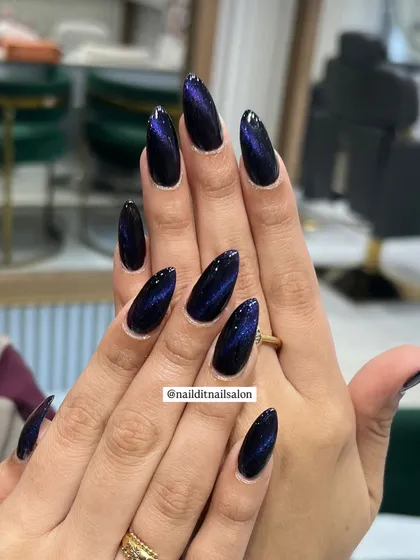 A deep galaxy effect created with magnetic cat-eye polish on long almond-shaped extensions. The dark base shifts with mesmerizing blue and purple light, offering a sleek and modern look that's perfect for any occasion.