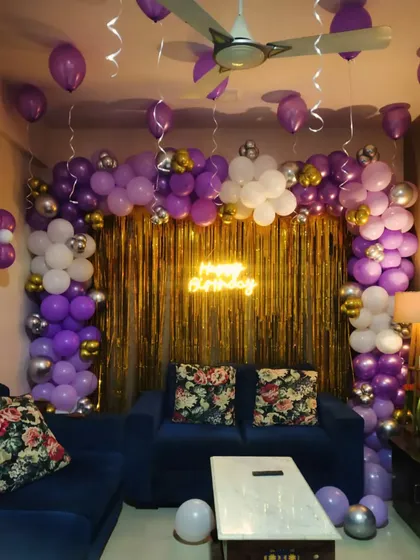 A purple and gold themed birthday decoration with a neon sign, set up in a cozy living room.