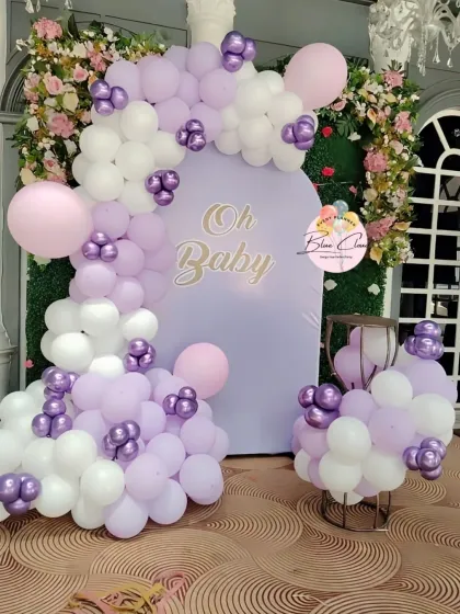 An elegant 'Oh Baby' shower setup with a lavender arched backdrop and a white and purple balloon garland.