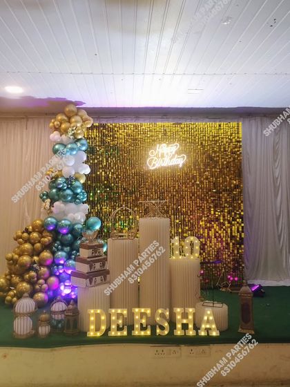 A grand party setup with a gold sequin wall, a multi-colored balloon tree, and light-up marquee letters for the name.