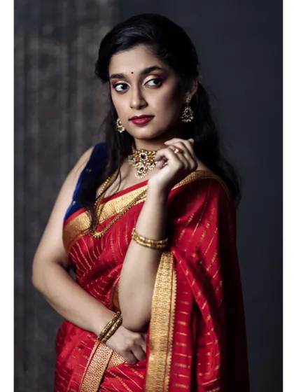 A classic three-quarter portrait against a dark, textured background. The model's confident gaze and the rich red of the saree make this a powerful and elegant image.