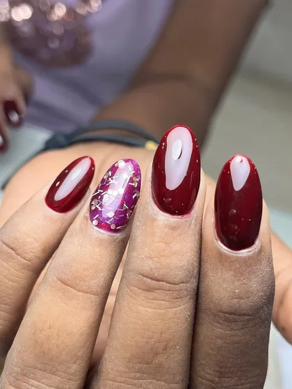 A beautiful wine-red manicure with a sparkling accent nail. The deep red is complemented by a nail filled with purple and silver glitter flakes for a touch of glamour.