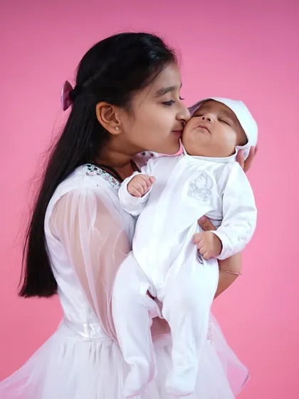 The special bond between siblings. An older sister gives her newborn baby brother a gentle kiss on the cheek, a truly precious moment captured forever.
