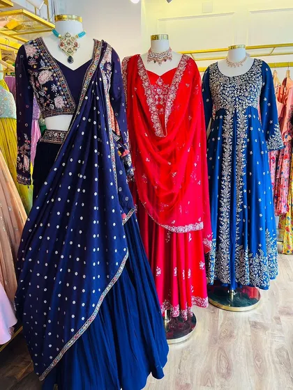 An in-store display of our jewel-toned festive wear, including a navy blue lehenga, a red anarkali, and a royal blue suit.