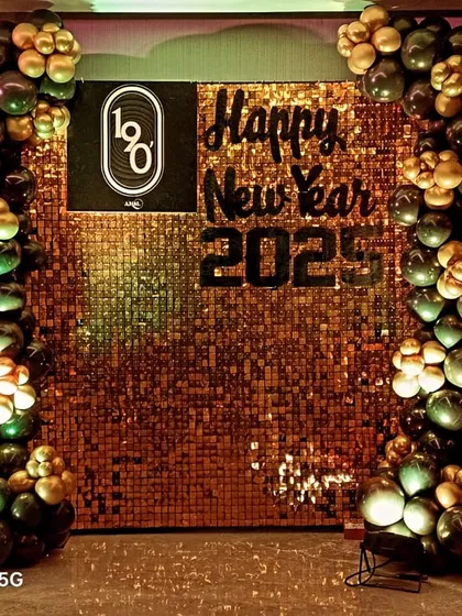 A New Year's party backdrop that also highlights the company brand. This design for '1o8' features their logo on a glittering gold sequin wall, framed by festive black and gold balloons.