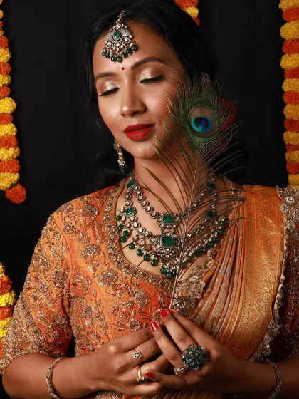 A serene and beautiful festive portrait. The peacock feather adds a touch of traditional symbolism, while the makeup with its green-toned jewellery and red lip is perfect for the occasion.