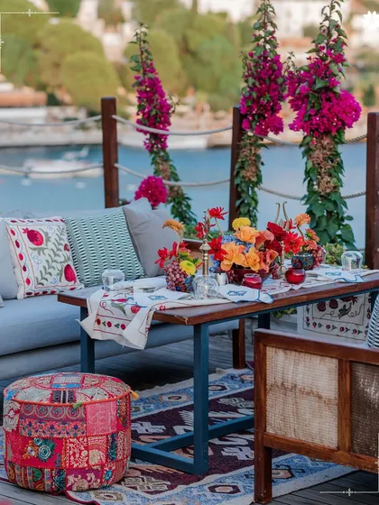 A vibrant, bohemian lounge setting by the sea in Turkey. The colourful textiles and fresh flowers create a relaxed yet celebratory atmosphere for a welcome event or mehendi.