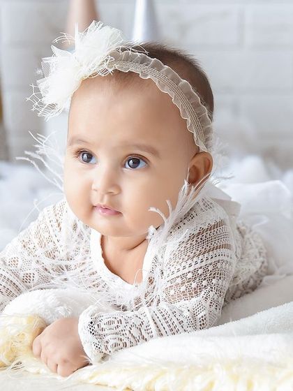 A delicate portrait of a baby girl on a soft, fluffy surface. The simple lace outfit and headband add just the right amount of detail.