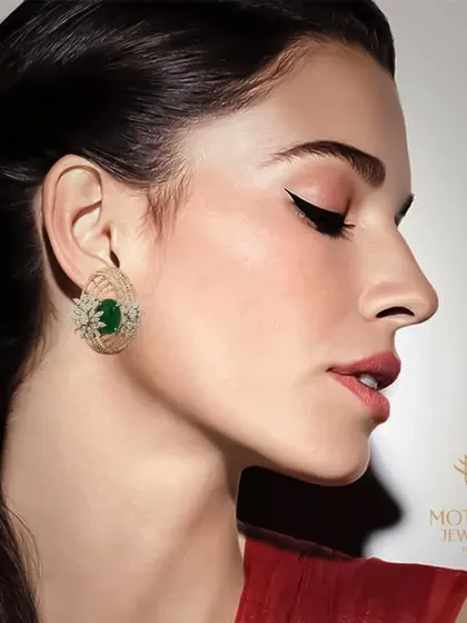 A model showcases a pair of elegant emerald and diamond stud earrings, highlighting their vibrant colour and classic design.