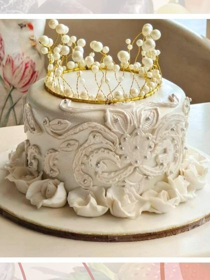 A regal white cake with intricate piping and a beautiful handmade pearl crown on top.