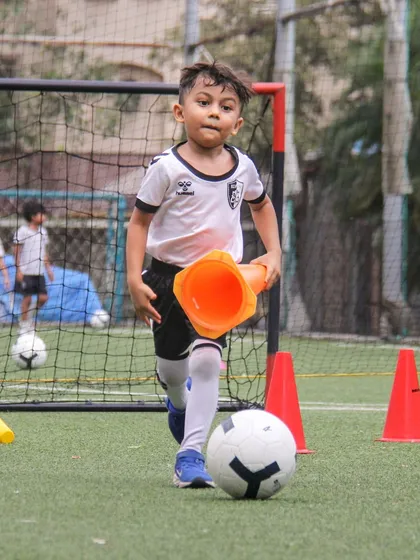 A young player runs with a cone while dribbling, a fun and creative drill we use to improve coordination and multitasking skills.