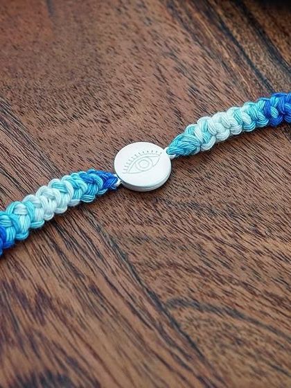 A product shot of the Silver Evil Eye Rakhi, with its beautiful blue ombre yarn and pearl details.