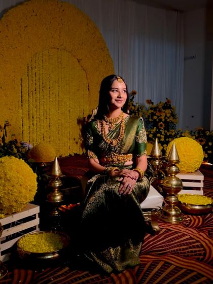 An elegant Haldi setup with a large circular backdrop made of yellow chrysanthemums. The bride is seated amidst floral spheres and traditional brass lamps.