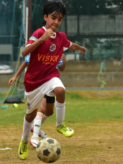 A player dribbling with speed and control, with a coach watching from the sidelines. Our players are always under expert guidance, even on match day.