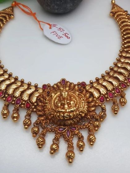 This 92.5 silver gold-plated temple necklace has a beautiful design with a central goddess motif. The necklace is adorned with ruby-colored stones and golden beads.