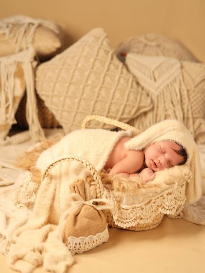 A cozy and neutral-toned boho theme. The baby, wearing an adorable bunny-eared hat, sleeps peacefully in a basket surrounded by soft, textured pillows and lace.