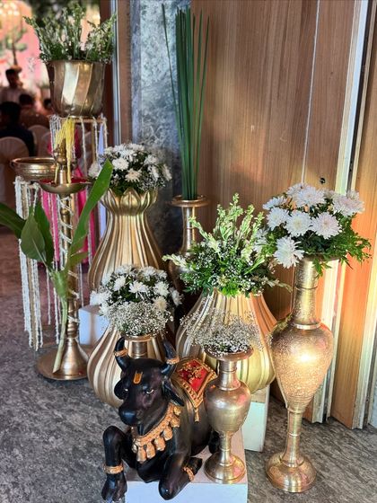 An artfully arranged corner with a Nandi statue, brass lamps, and golden vases filled with white flowers, showcasing a blend of textures and tradition.