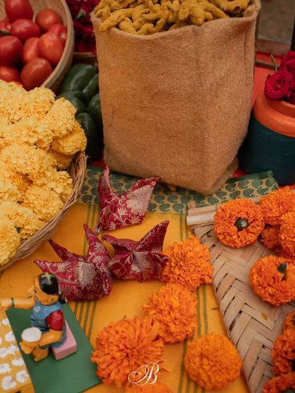 A close-up of the origami birds and Channapatna toys arranged on a vibrant yellow cloth with marigolds, part of a larger, eco-friendly decor installation.