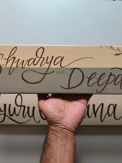 A close-up of the "Aishwarya and Deepak" name plaque. The two-tone background and delicate, hand-painted leaves add a touch of nature-inspired elegance.