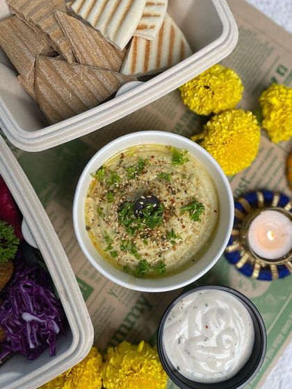 A closer look at our creamy hummus, garnished with parsley and sesame seeds, served with a side of dip. It's the star of our Pita Hummus platter.