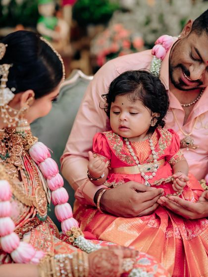 A family captured during a ceremony. The baby girl's red pattu pavadai, with its delicate gold embroidery, was custom-made to be the star of the show.