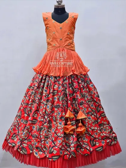 An elegant Kalamkari lehenga with a red floral print. The orange peplum blouse has delicate embroidery.