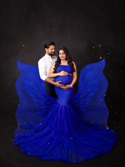 A dramatic maternity portrait using a deep blue gown against a dark backdrop. The added sparkle effect gives this image a magical, fairytale quality, perfect for a fine-art look.