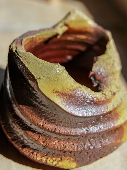 The dramatic lighting on this wood-fired piece highlights its sculptural quality. The textures are deep and inviting, a landscape captured in clay.