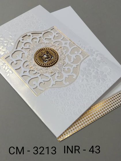 An elegant white invitation with a laser-cut window and a gold emblem. The design is clean and sophisticated, with a touch of sparkle from the gold foil border.