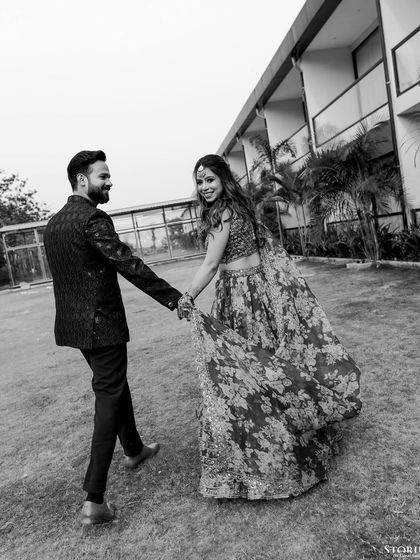 A playful black and white shot of Amrit and Akarshika, as she leads him by the hand, looking back with a smile.