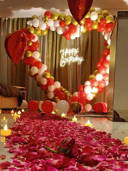 A romantic birthday surprise we set up in a client's room. We transformed the space with a heart-shaped balloon arch, a custom "Happy Birthday" neon sign, and a candlelit path of rose petals leading to the bed.