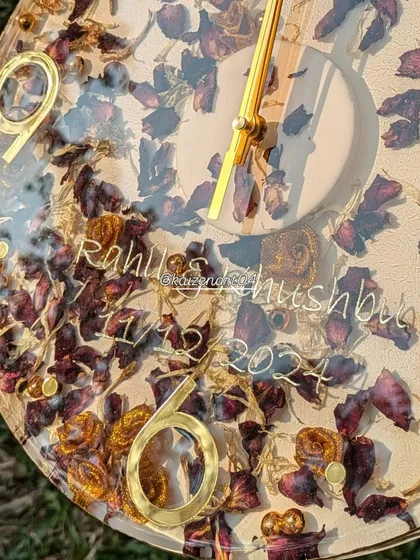 A detailed shot of a 12-inch wall clock, showing the preserved rose petals and the couple's names and wedding date elegantly scripted on the clock face.