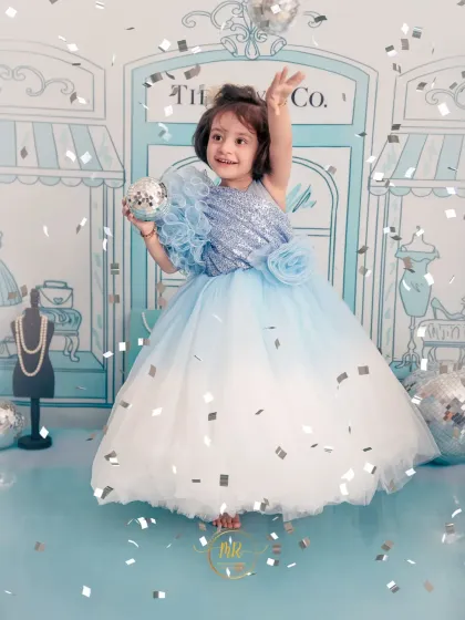 A playful and stylish toddler photoshoot with a "Tiffany & Co." theme. The little girl is dressed in a beautiful blue gown, tossing confetti and celebrating in a custom-designed set.