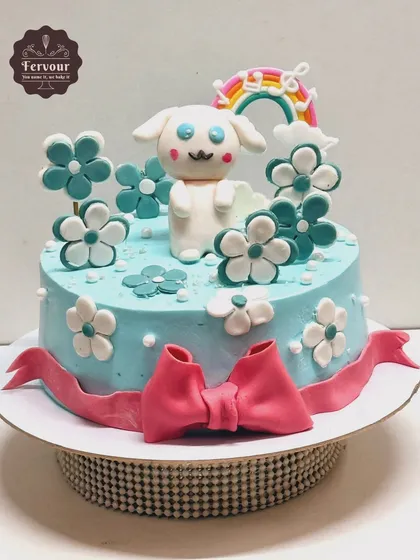 A sweet Cinnamoroll theme cake. This light blue cake is decorated with a cute fondant Cinnamoroll character, flowers, and a rainbow, making it an adorable choice for a birthday.