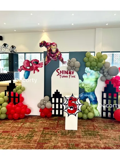 A wider shot of the Avengers party setup, showing the arrangement of the backdrop panels, balloons, and props in the event space.