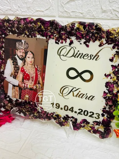 A 9x12 inch resin frame with a zig-zag border, preserving dark purple flowers around a wedding photo. The couple's names and date are displayed in elegant gold script.