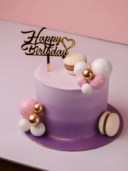 We love creating sweet and simple cakes like this purple ombré design. The layers fade from rich violet to soft lavender, creating subtle elegance, and it's finished with macarons and decorative spheres.