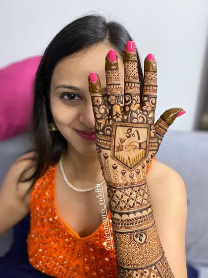 A happy bride showing off her beautiful henna. This design features a central panel with a fish motif, surrounded by dense, traditional patterns covering the hand and arm.